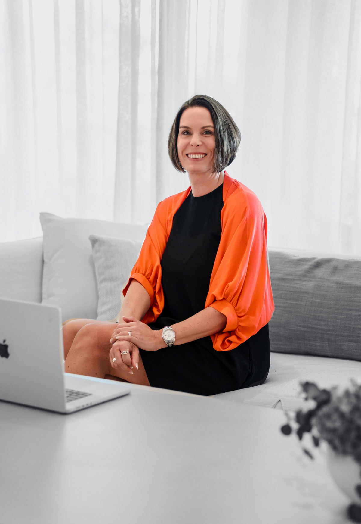 Dossier Hypnose CTA Christiane Baumann sitzt auf dem Sofa mit Laptop und lacht in die Kamera